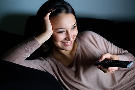 a woman lays on the couch watching television