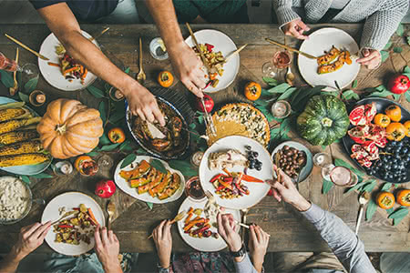 friends pass savory dishes over a Thanksgiving table